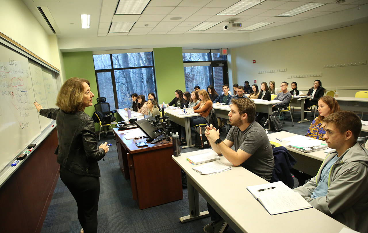 Grace Zimmerman pointing to white board teaching a class