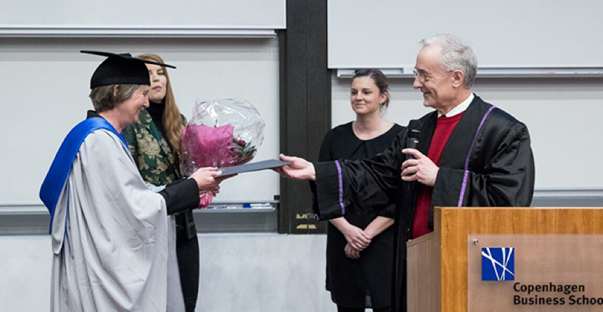 Graddy on stage in regalia with flowers receiving diploma