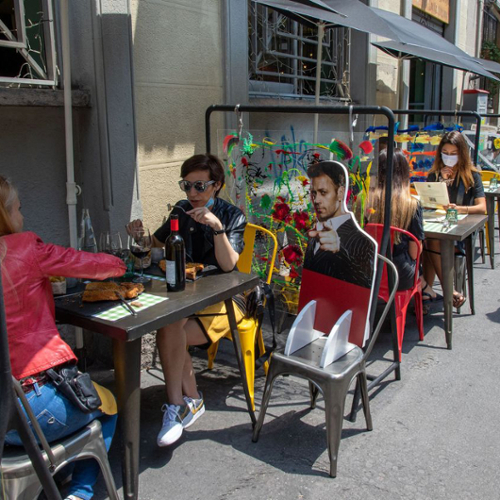 People eating on a patio next to a cardboard cutout of a person in a chair.