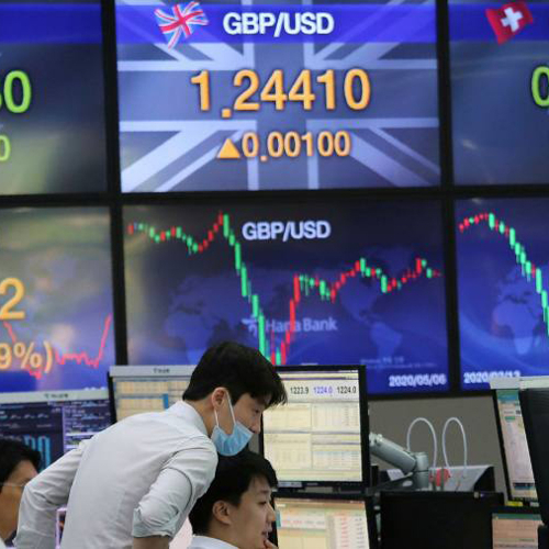 Image of two traders in front of a giant electronic board showing exchange rates.