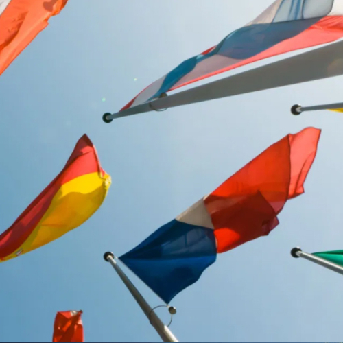 A shot looking up at a few countries' flags flying against a clear sky.