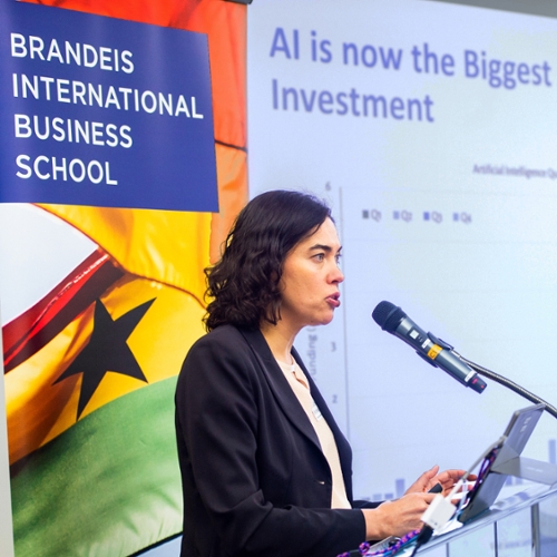 Prof. Anna Scherbina speaking at a podium with the school logo in the background.