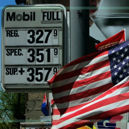 An American flag waving in front of a gasoline price sign showing prices over $3 per gallon.