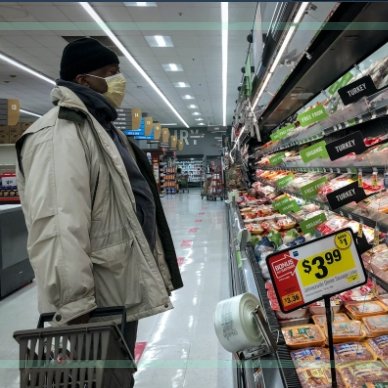 A man in a supermarket stands in an aisle examining the meat cooler.