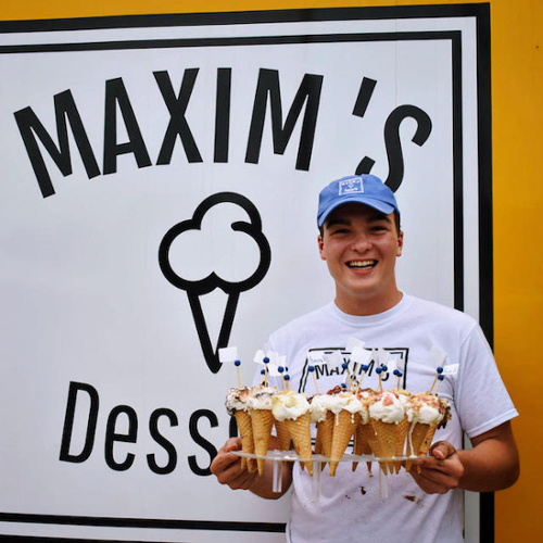 Max LeBlanc holds pie cones in front of a bit white Maxim's Desserts sign.