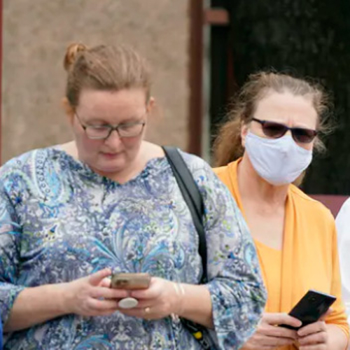 Two people outside in line, one with a mask and one without.