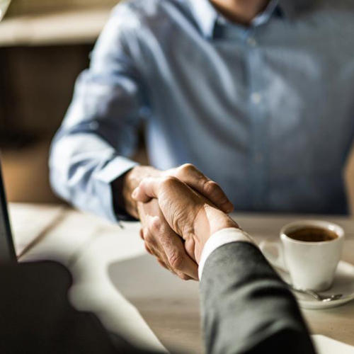 A photo of two men shaking hands over coffee.