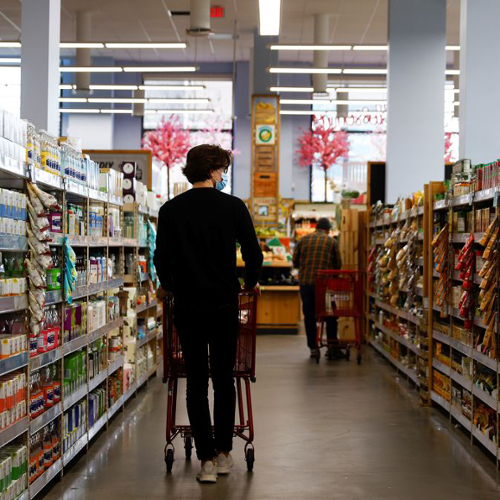 A shot of the back of a shopper pushing a cart down an aisle at the grocery store.