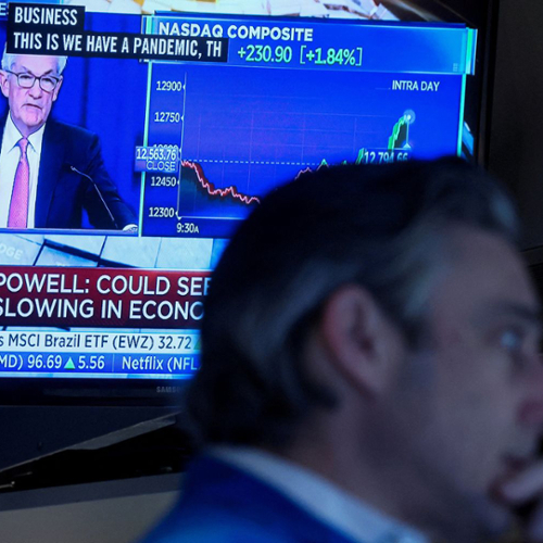 Fed Chair Jerome Powell appears on a screen behind a man working at a desk.