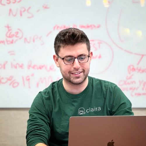 Elan Kawesch sitting at a table working on a laptop, with a whiteboard behind him with notes and ideas.