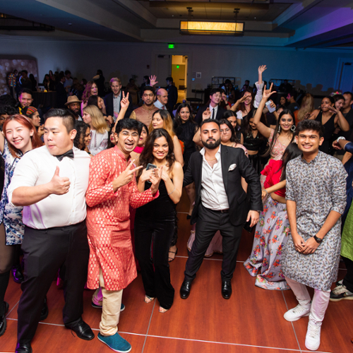 Students in traditional and modern dress dance on the dance floor in blue strobe lights.