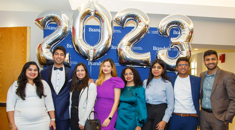 Students pose in front of a Brandeis backdrop with golden 2023 balloons.