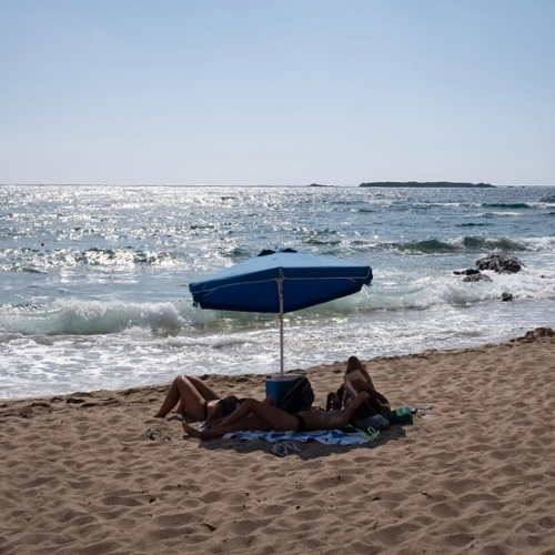 A shot of people lying on a towel under an umbrella at the beach.