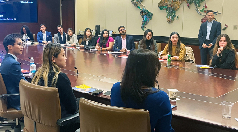 Students on the Industry Trek to BlackRock sit around a large conference table listening to finance professionals.