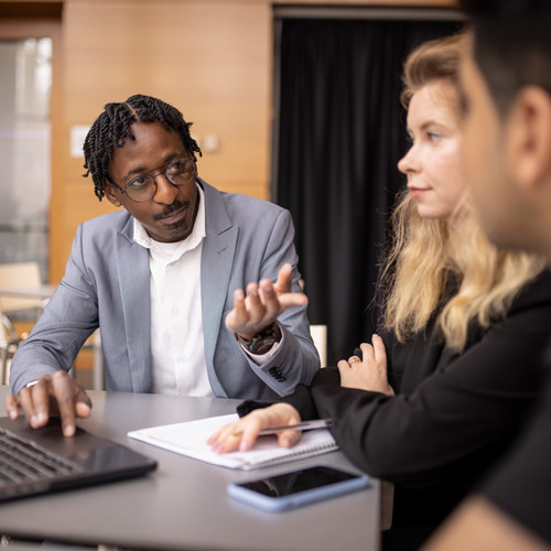 George Nakwaya talks to two other students while using a laptop.