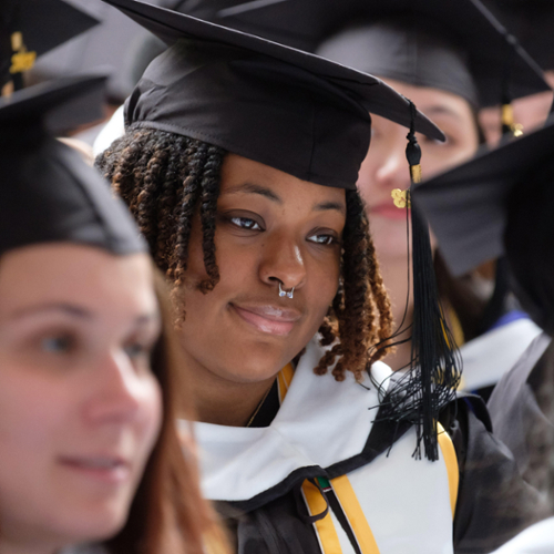 A graduate in full regalia smiles as she waits to be called up for her diploma.