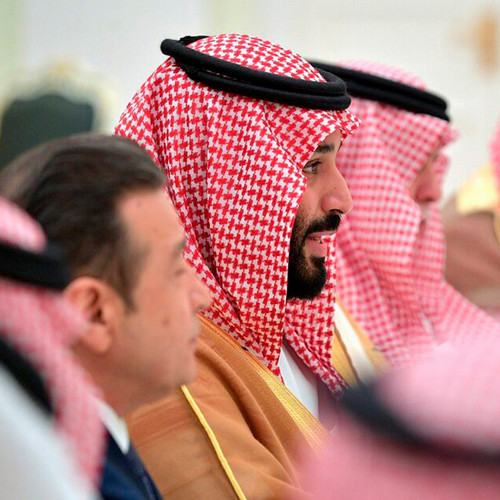 A photo of Saudi Finance Minister Mohammed al-Jadaan sitting at a table wearing a red houndstooth keffiyeh with two black agals.