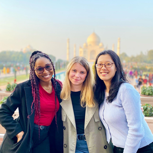Three students pose for a photo with the Taj Mahal in the background.