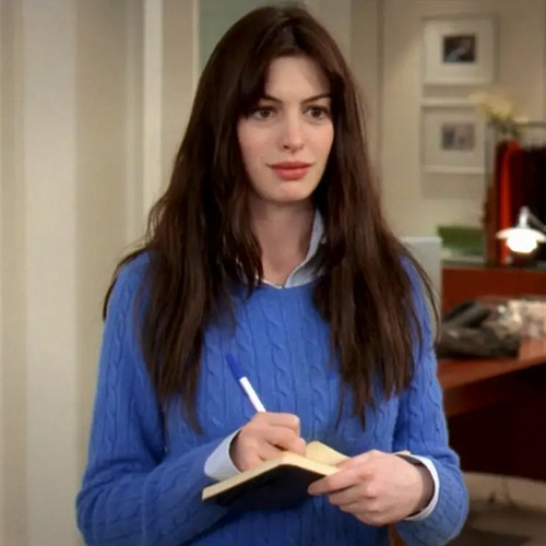 A young woman in a blue sweater stands with a notebook and pen taking notes.