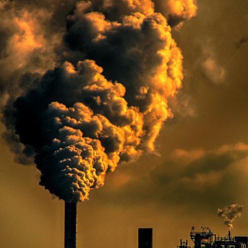 A sepia photo of a smokestack emitting a wide cloud of smoke.