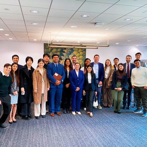 Nearly two dozen students in business dress pose for a picture with alumni and managers in the lobby of HSBC.