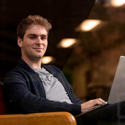 Ephriam Zimmerman sits with a laptop on his lap smiling at the camera.