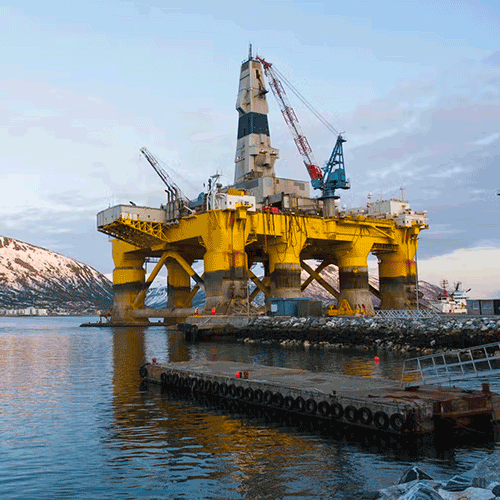 A yellow oil platform in a fjord with a red ship nearby.