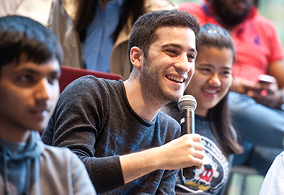 A student smiling asking a question with a microphone in crowded room