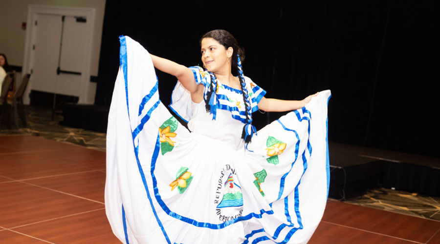 A student shows off her white dress with blue trim, bringing up the ends by holding out the hem with arms to her side.