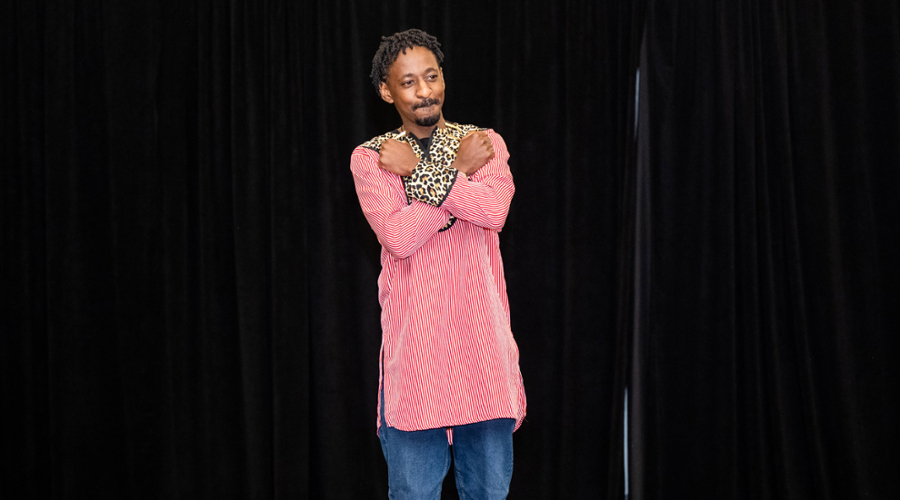 A student wearing a red and white striped shirt with leopard print lapels and cuffs crosses his arms on the runway.