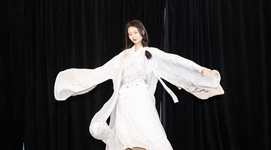 A student stretches her arms to open the flowing fabric on the sleeves of her white dress with white and gray embroidery.