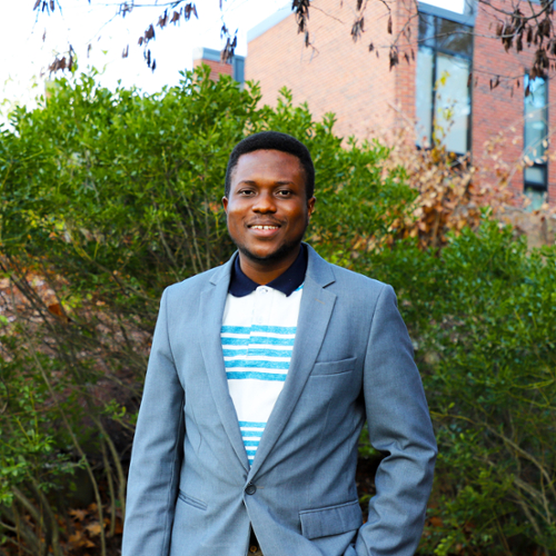 A portrait of Jonathan Korash in a white and blue striped shirt under a gray suit coat.