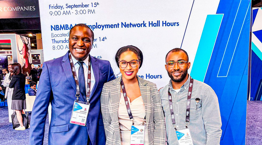 Three students pose in front of the National Black MBA Association backdrop.