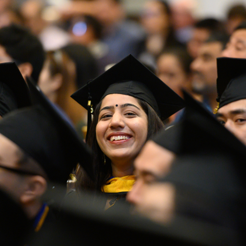 A graduate in her cap and gown smiles in the crowd at commencement.