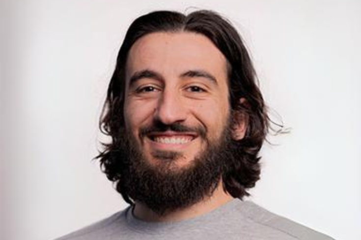 Headshot of Eric Moyal. He is smiling at the camera in front of a pale grey background. 