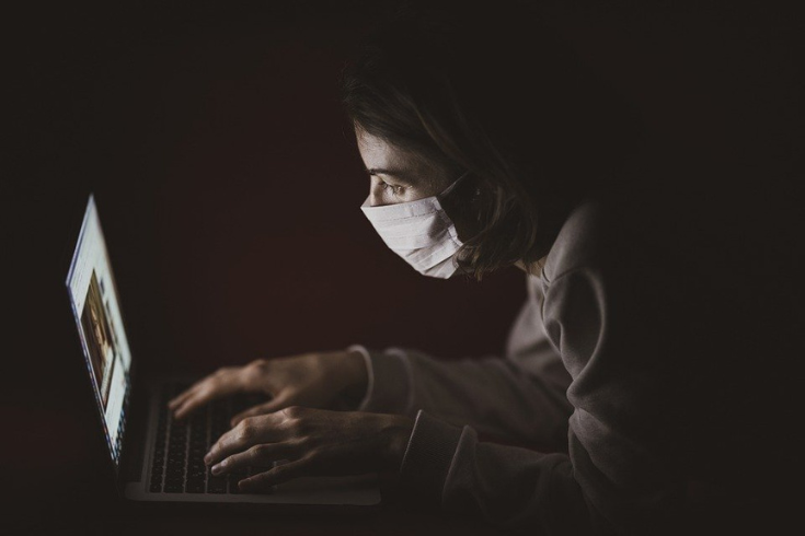 Person wearing a mask while typing on a laptop in the dark