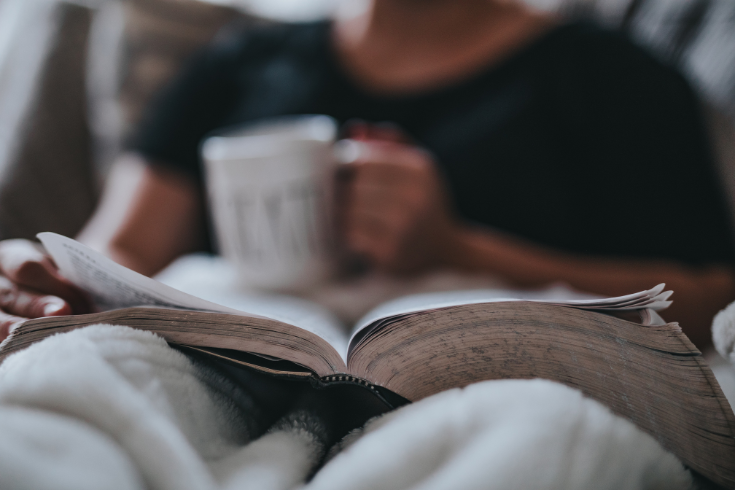 Person reading a book, holding a cup of tea.