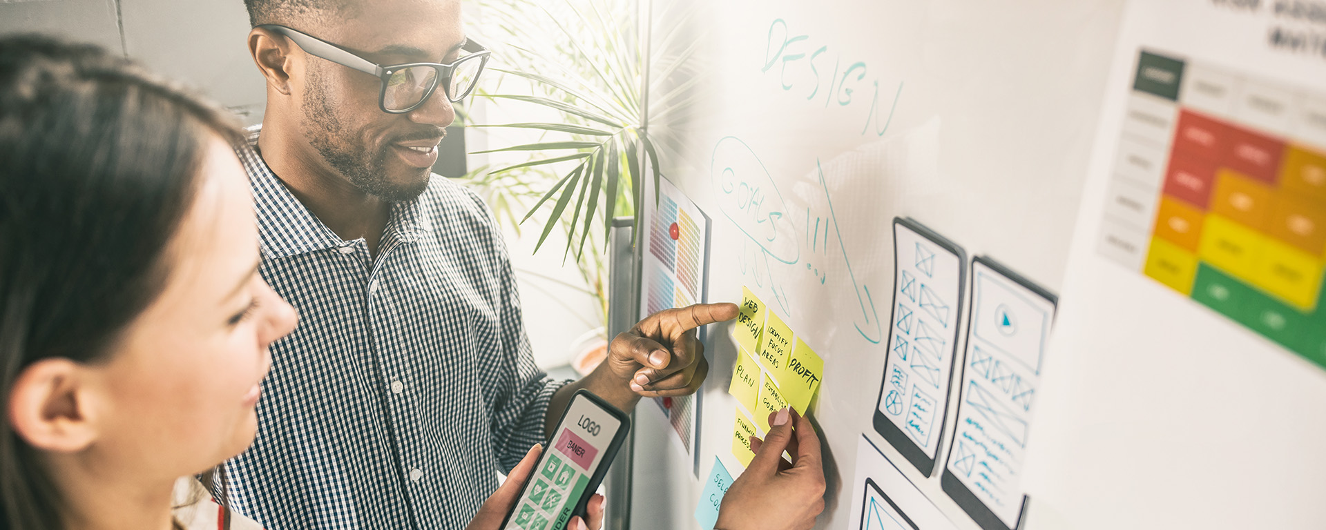 Two people look at stickie notes on a whiteboard
