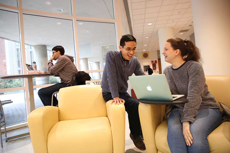 Two students laugh while talking and looking at a computer