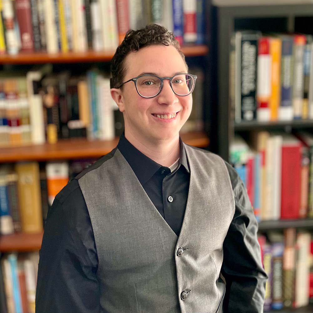 Headshot of Cole Ayasse in front of bookshelves