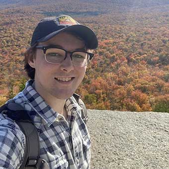 Hayden McCormick stands overlooking mountains and many autumn trees.