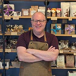 Jeremy Spindler, wearing an apron, stands in front of shelves of candy.