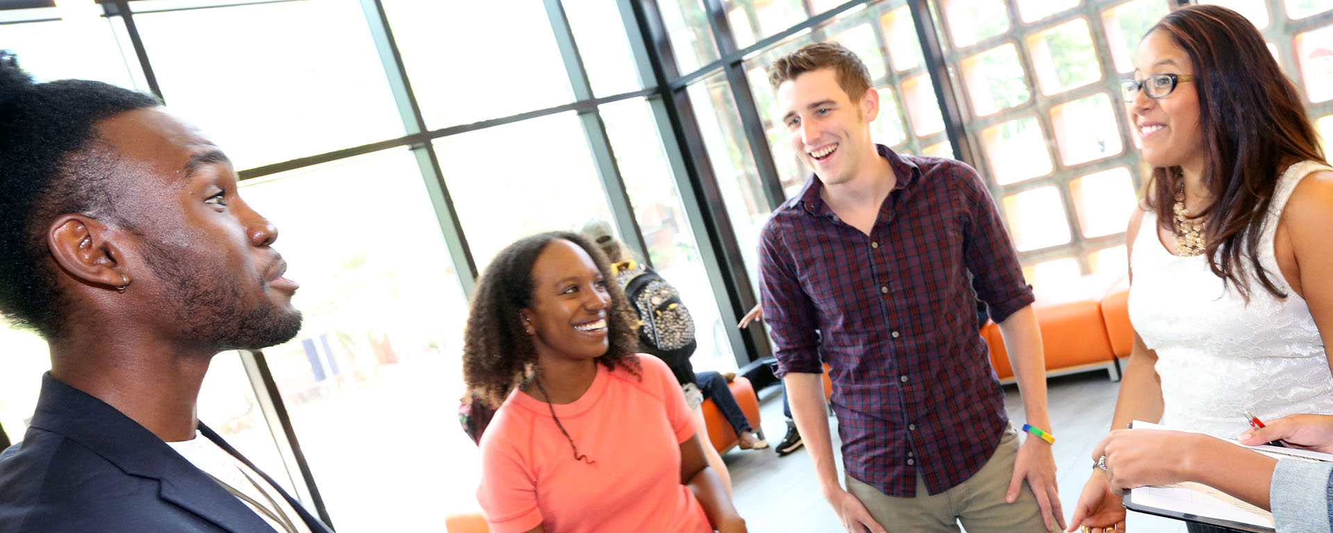 three grad students chatting and smiling while seated in brightly lit room