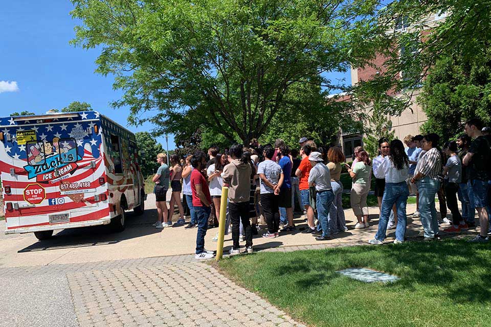 A large group of people line up outside next to an ice cream truck.