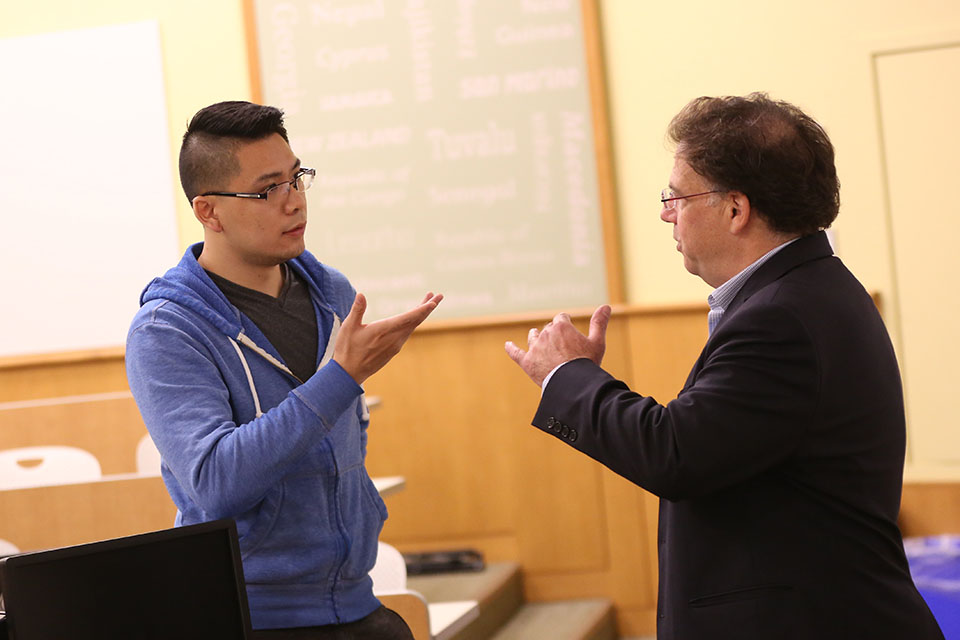 international business school students speaks with faculty member after class