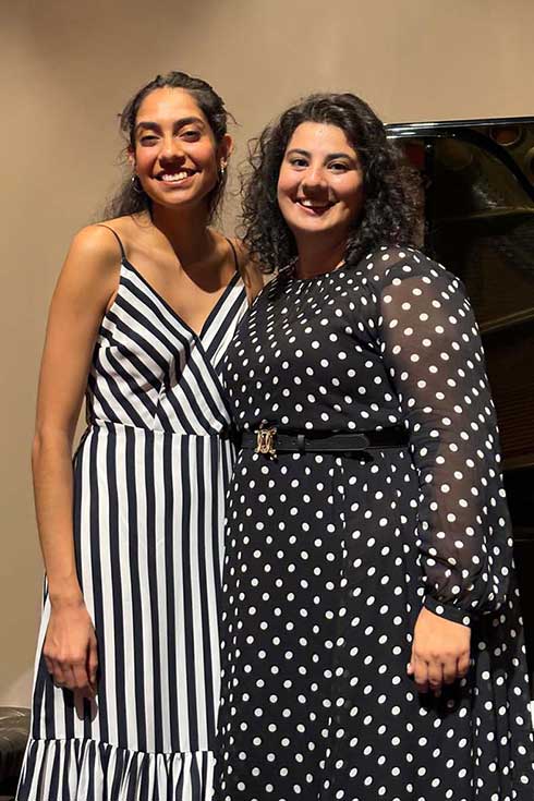 Mariel Mayz and Alexandra Burkot stand in front of a piano.