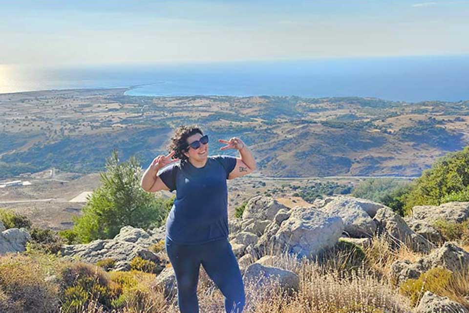 Alexandra Burkot poses on a mountaintop, making two muscles.