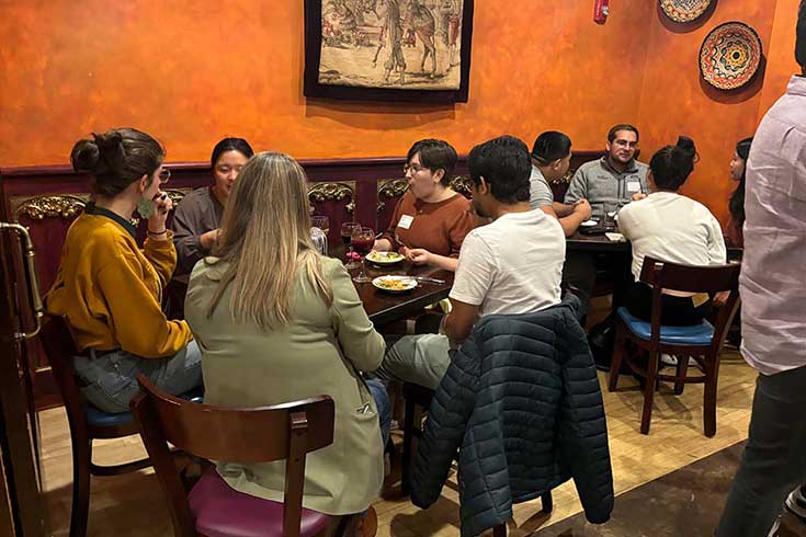 People sit in groups at tables, talking and eating.