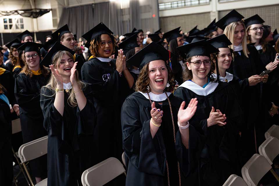 Students in Commencement robes stand and applaud.