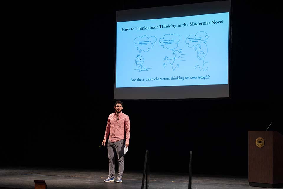 Daniel Schwartz stands onstage, presenting in front of a slide.